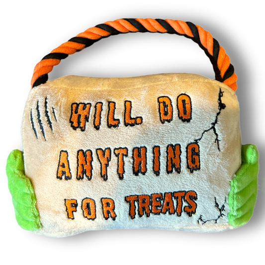 A halloween themed plush dog toy that resembles a sign with a rope. Green hands hold the sign and the sign reads "Will Do Anything For Treats".